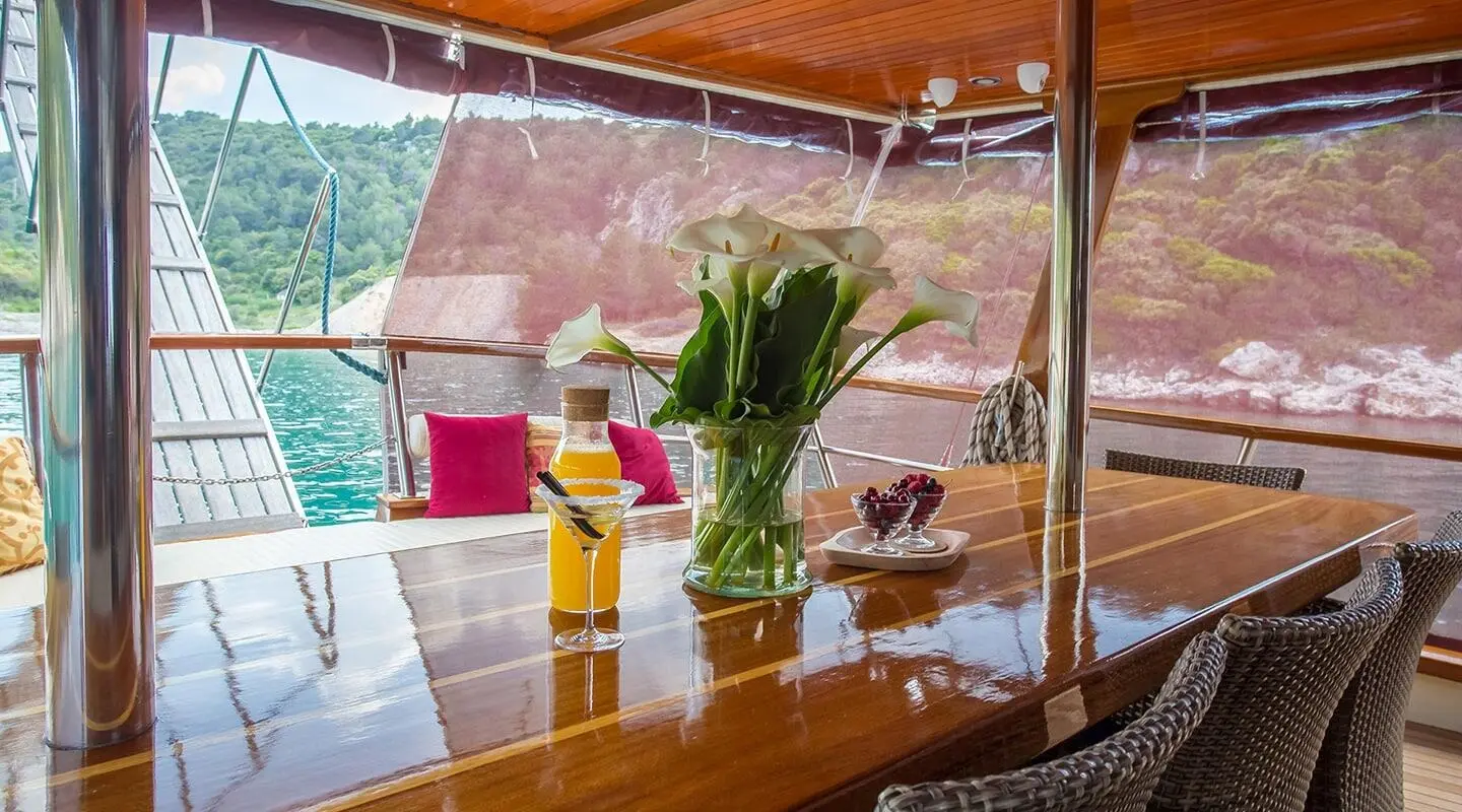 Sunset yacht Altair with a wooden deck, potted plants, and calm blue water