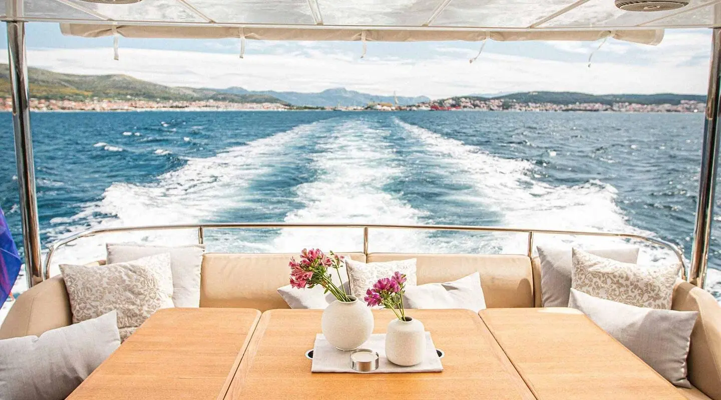 A luxurious yacht deck with a table, flowers, and seating, speedboat wake beyond