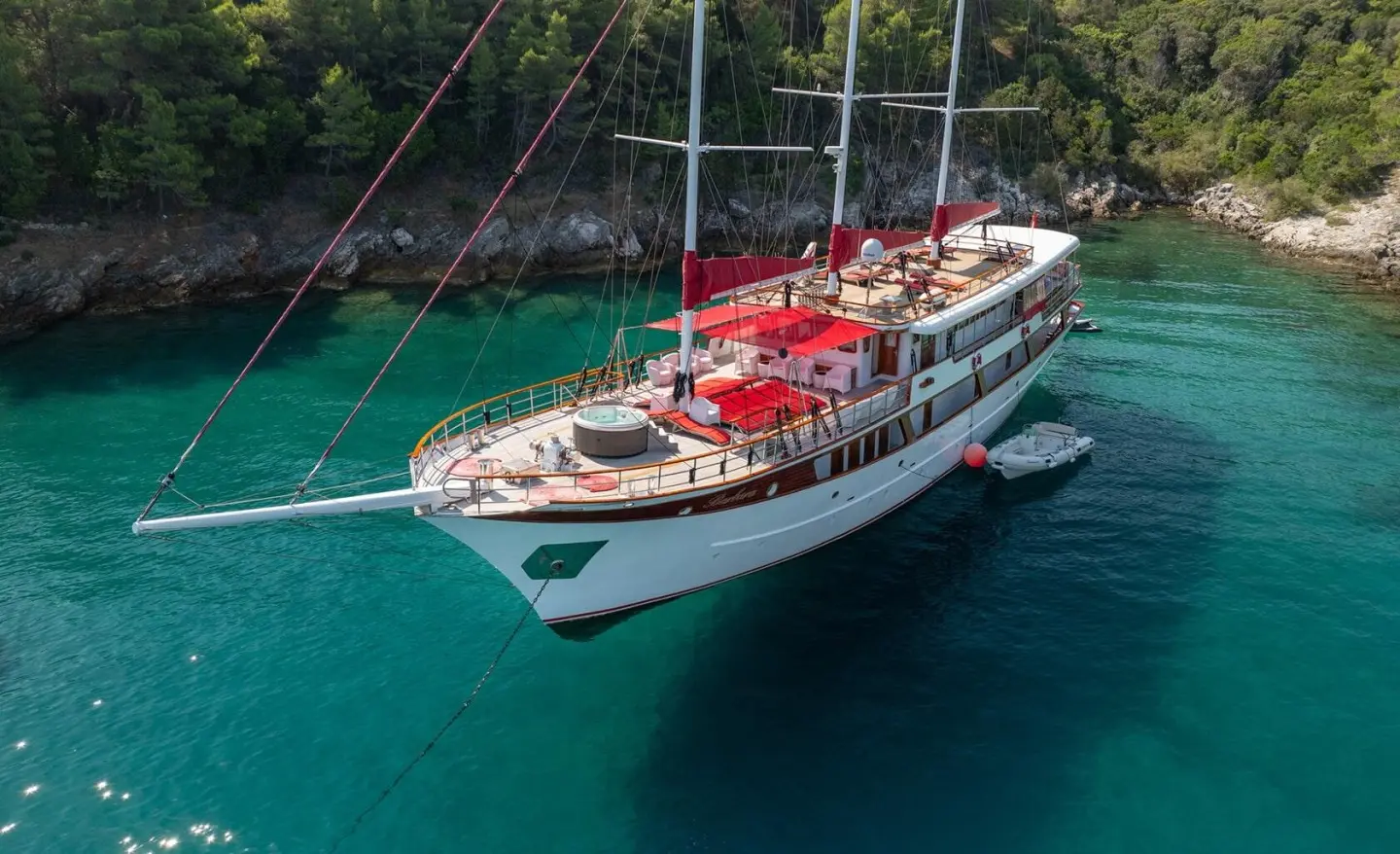 Yacht Barbara anchored near turquoise water with red deck seating and sails up