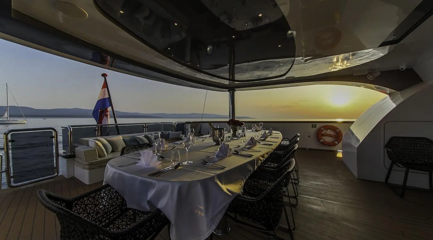 Omnia yacht aft deck dining setup under shade at sunset with table setting