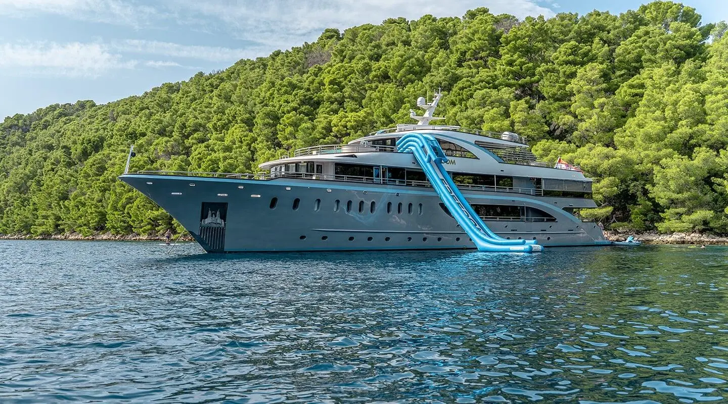 Yacht Freedom with a bright blue water slide along a rugged green hillside