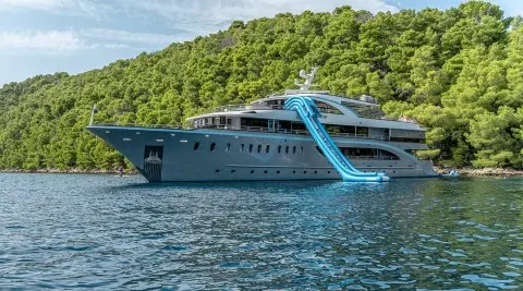 Yacht Freedom with a bright blue water slide along a rugged green hillside