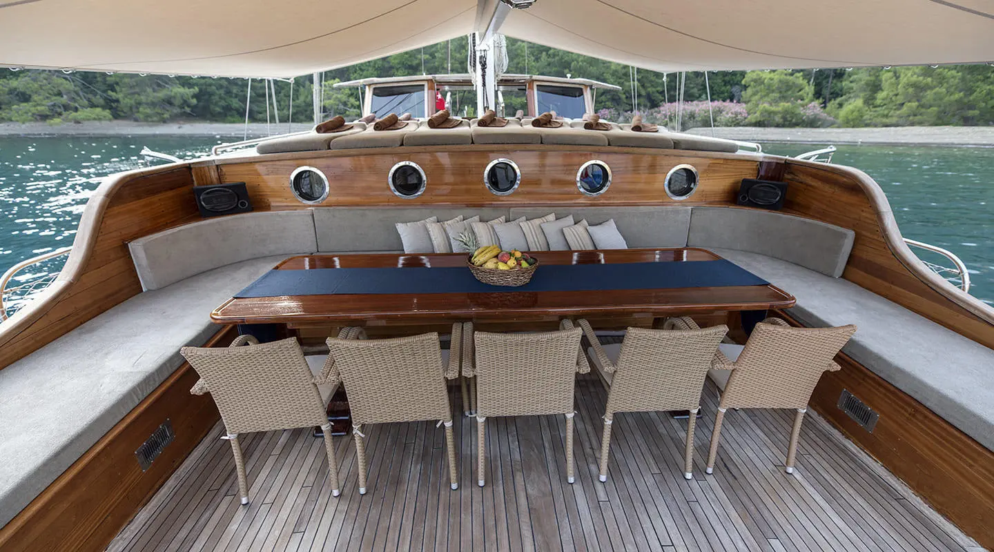 Kayhan 8 yacht outdoor dining area with wooden deck and cushioned seating under shade