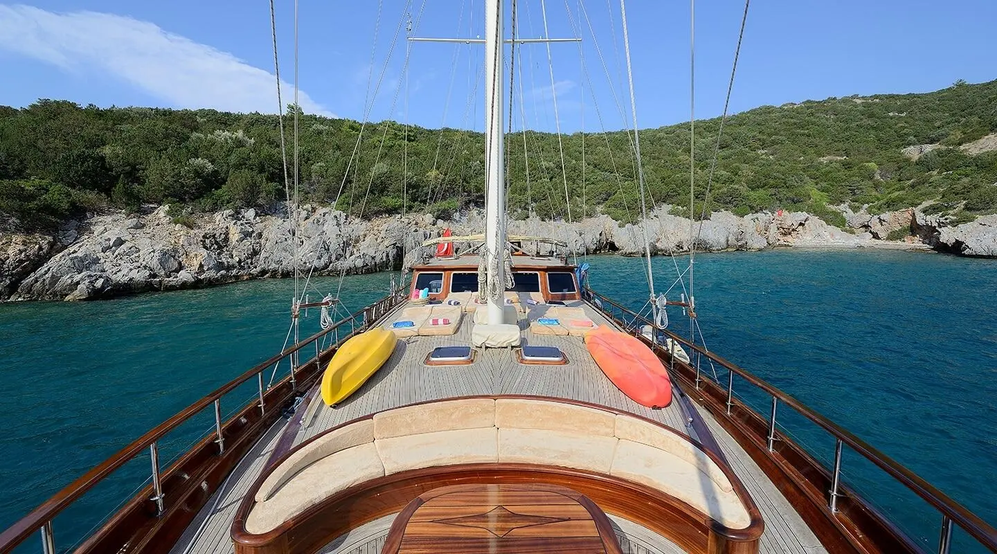 View from the bow deck of a yacht with kayaks on the deck and rocky shoreline
