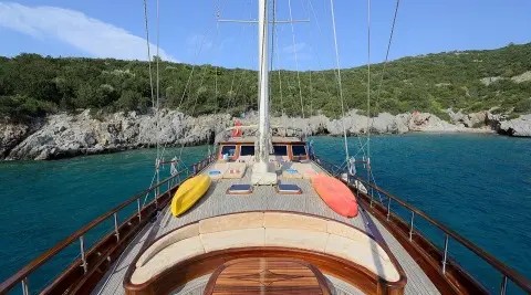 View from the bow deck of a yacht with kayaks on the deck and rocky shoreline