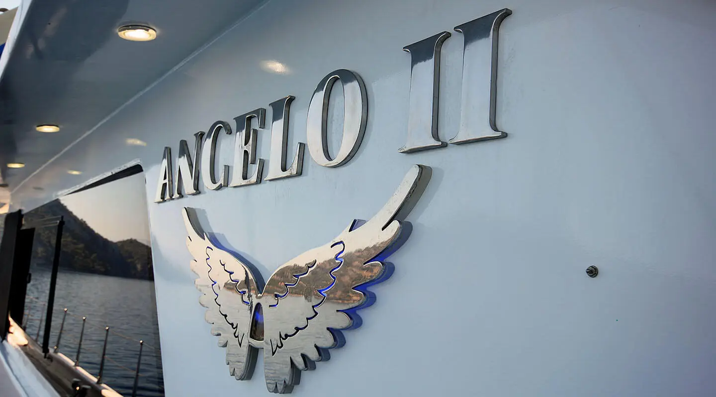 Angelo II yacht name and silver wing emblem on light blue hull exterior
