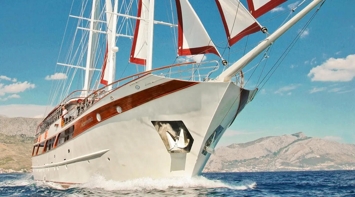 Amorena motor yacht cutting through blue sea with sails in background