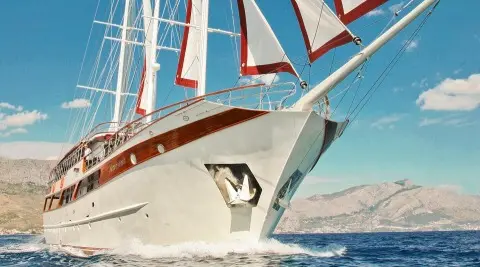 Amorena motor yacht cutting through blue sea with sails in background