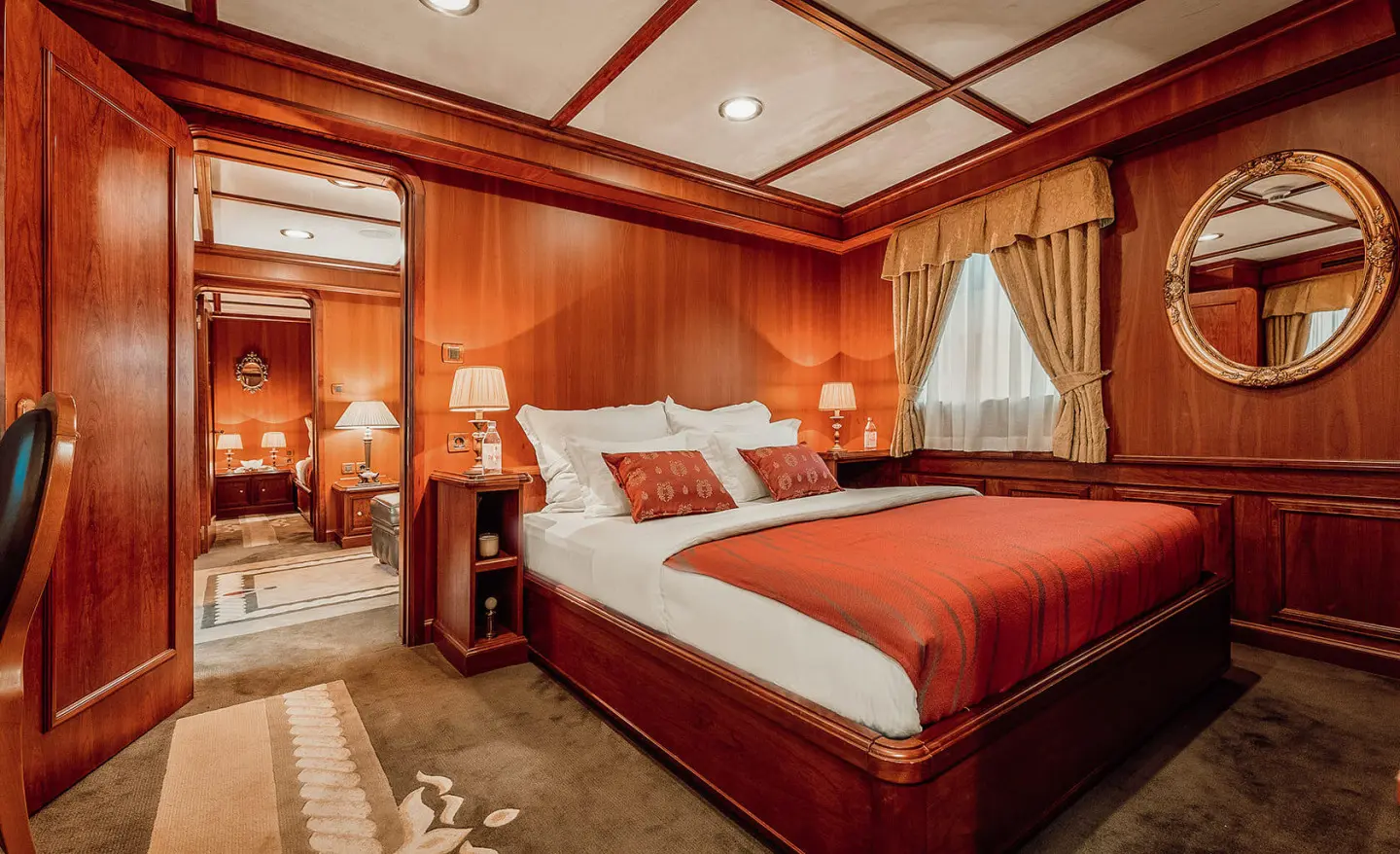 Seagull II luxury yacht cabin with wood paneling, red bedspread, and bedside lamps