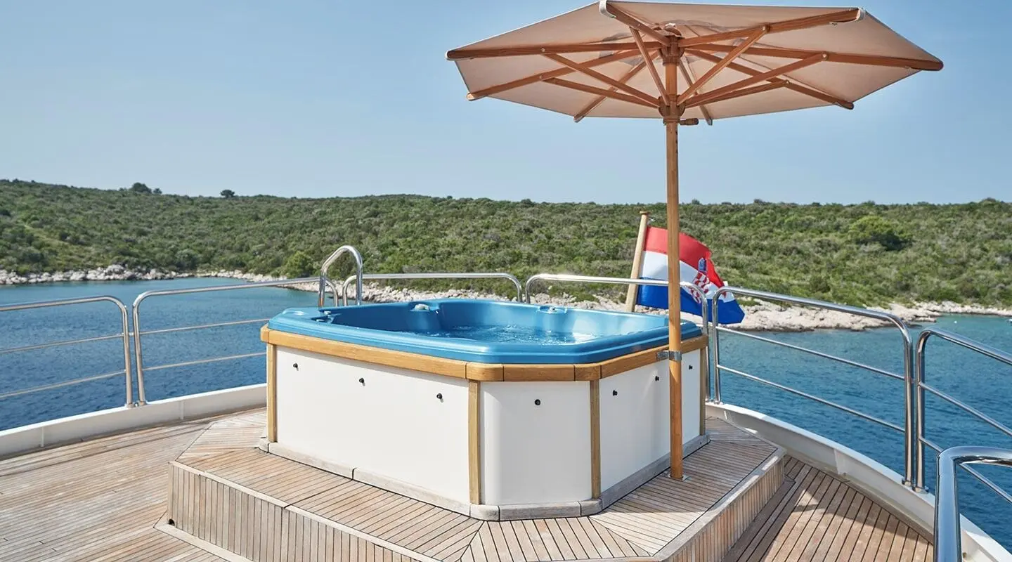 Yacht La Perla on clear blue water with a hot tub on deck and umbrella