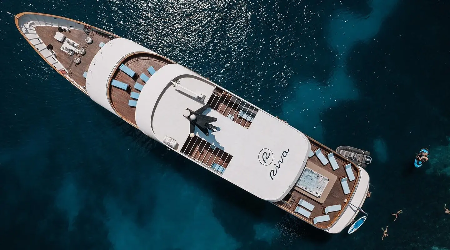 Top-down view of a white Riva luxury yacht anchored in blue water, deck visible