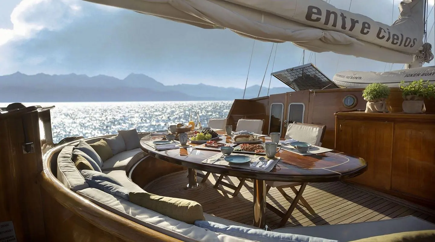Gulet Entre Cielos on aft deck with table and chairs overlooking coastal view