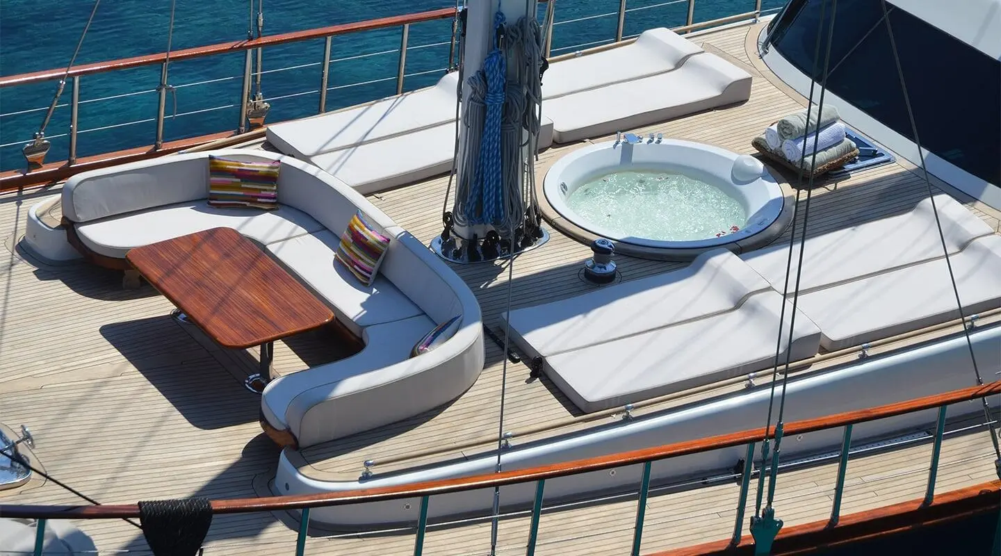 Blue Heaven yacht deck with seating, ropes, and blue sail at sunset harbor