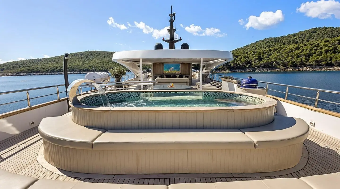 Bella yacht deck with lounging sofas, stairs to water, sunny harbor backdrop