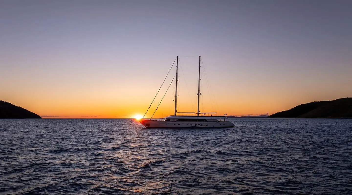 Sunset over calm sea with a sleek yacht silhouette near horizon