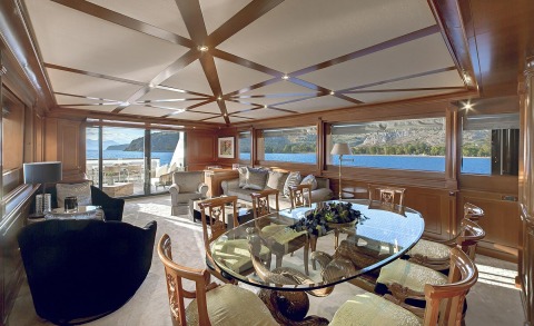 Aquila luxury motor yacht interior with wood paneling, large windows, glass dining table and upholstered seating