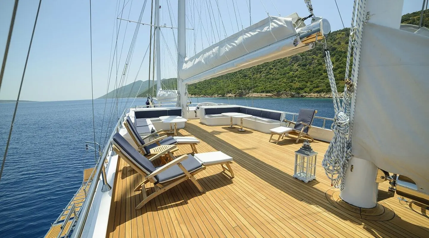 Bella Mare yacht deck with teak wood, lounge seating, and sails on a calm blue sea