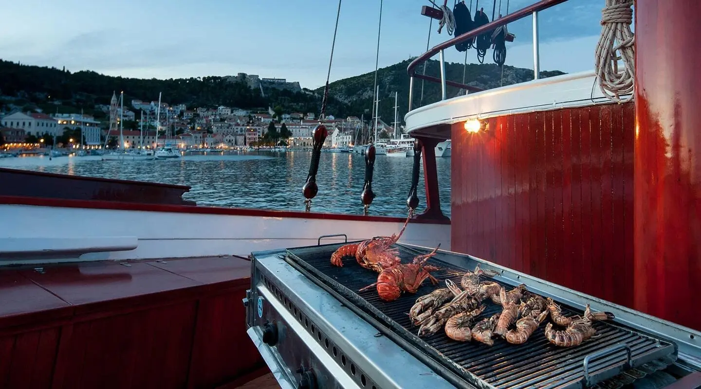 Romanca yacht deck with railing and sunset-lit harbor, seafood on tray