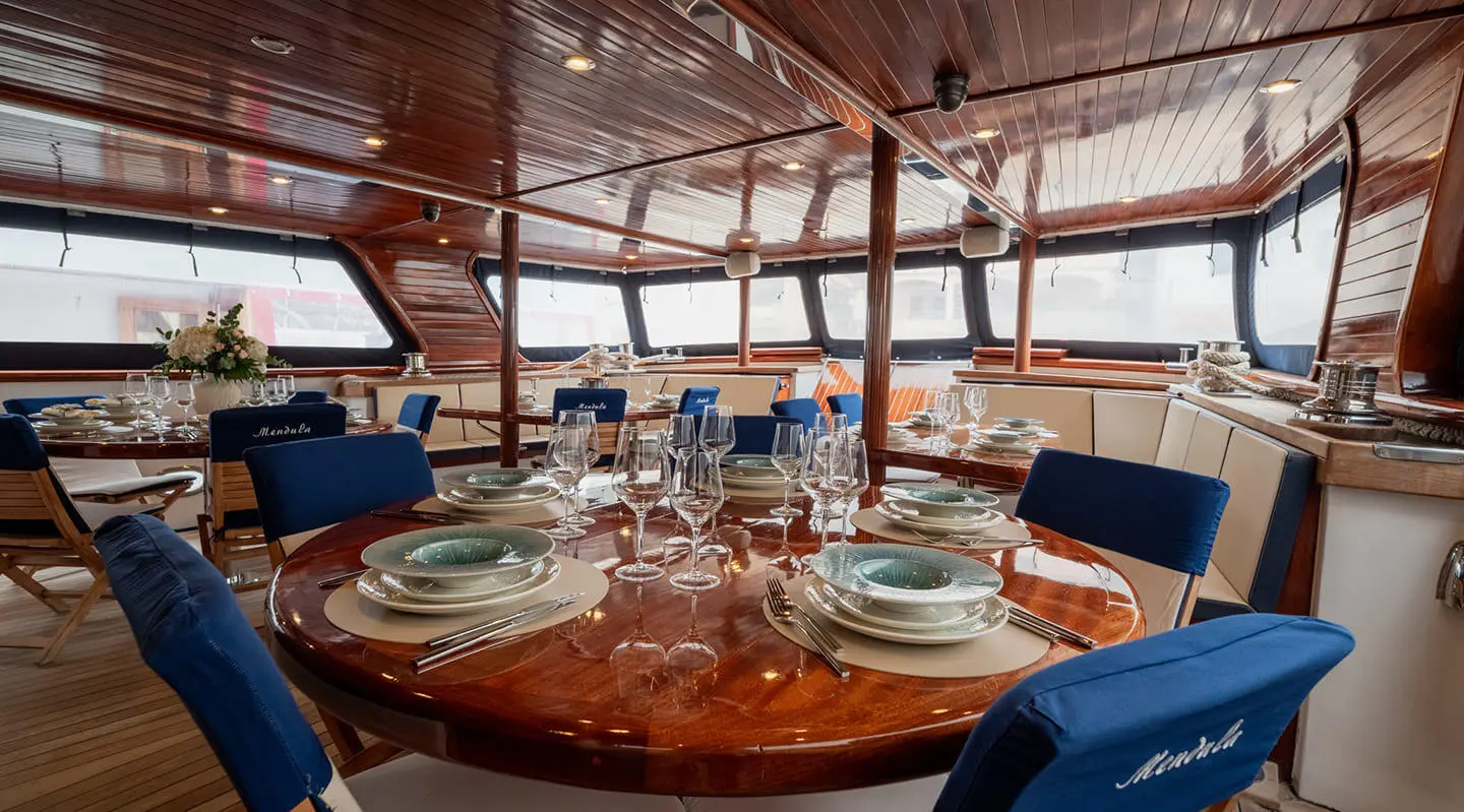 Mendula yacht dining on deck with sunset view through rigging and blue cushions