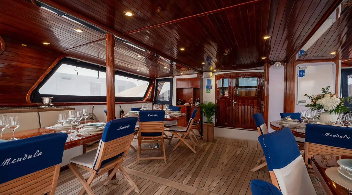 Mendula yacht on deck with blue cushions and elegant dining area at sunset