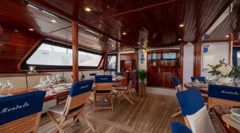 Mendula yacht on deck with blue cushions and elegant dining area at sunset