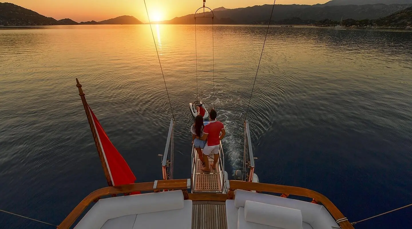 Blu Dream yacht deck at sunset with two people on bow, calm sea