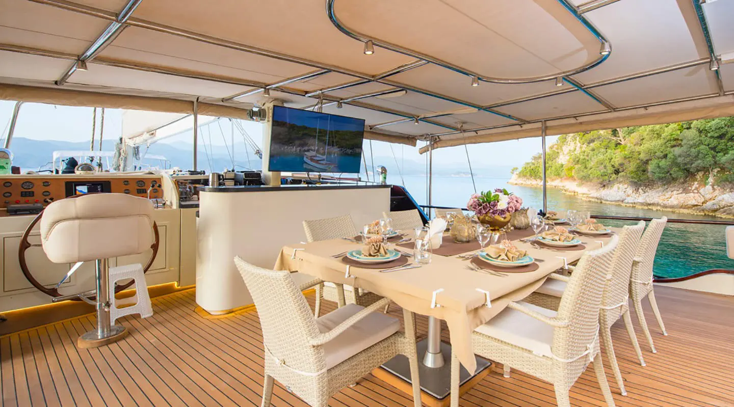 A gulet-style yacht deck with white chairs and a dining table set under a canopy
