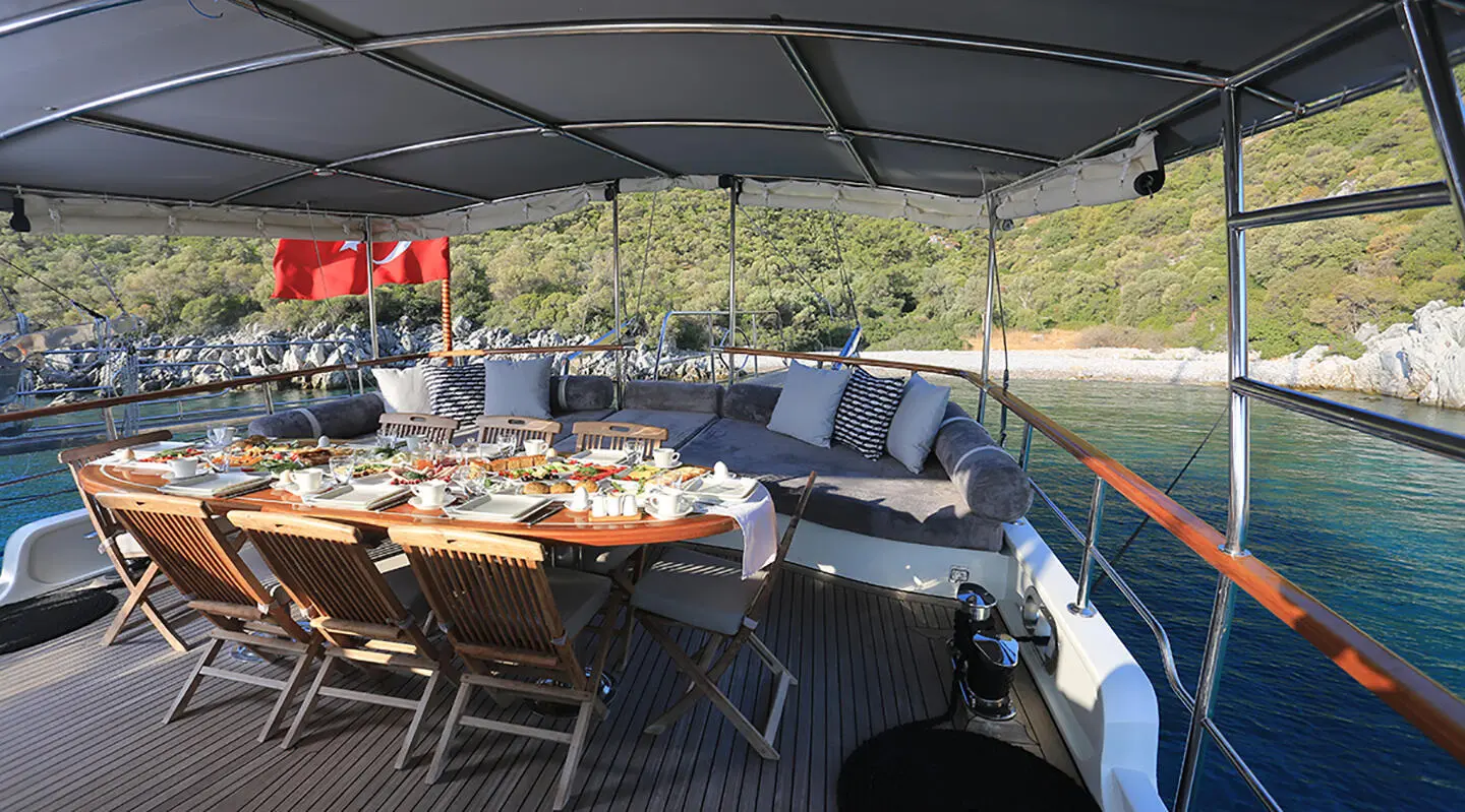 Under a shaded deck view, a dining table set with dishes aboard a sleek blue yacht
