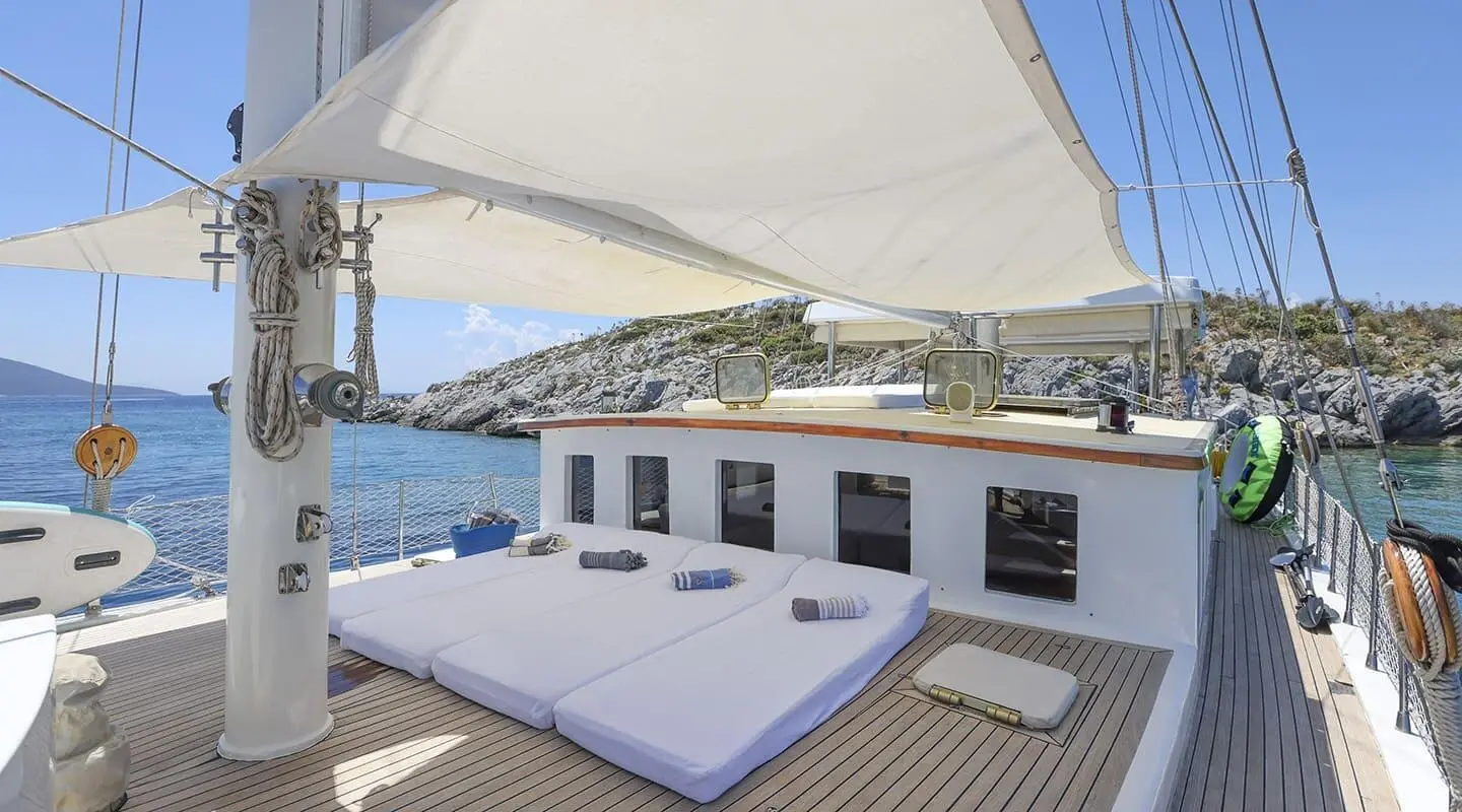 Gazella yacht deck with sun loungers and sail in bright blue sea sunset