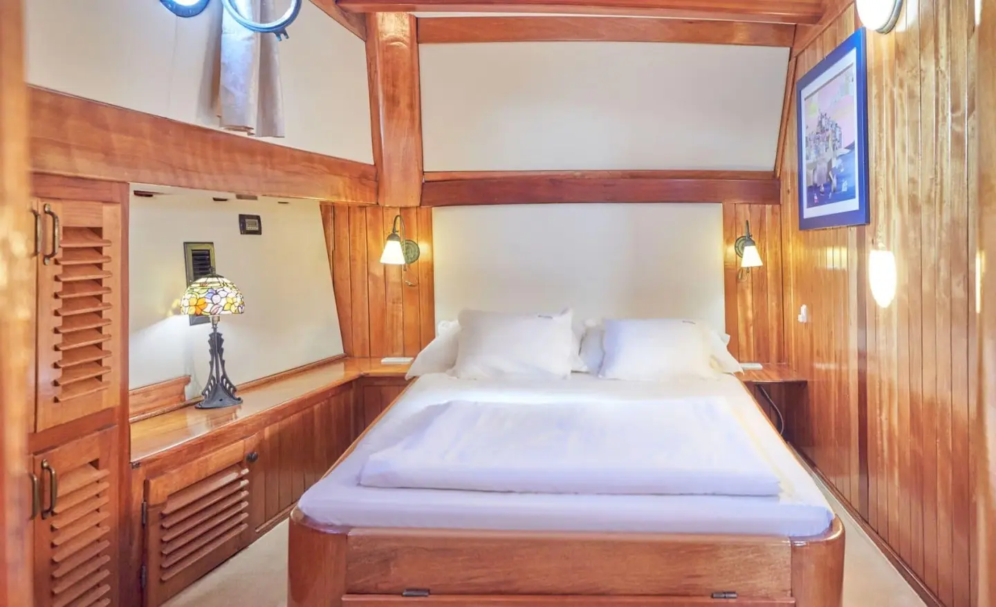 Cozy master cabin aboard Libra yacht with large bed, wooden shelves, and soft lighting