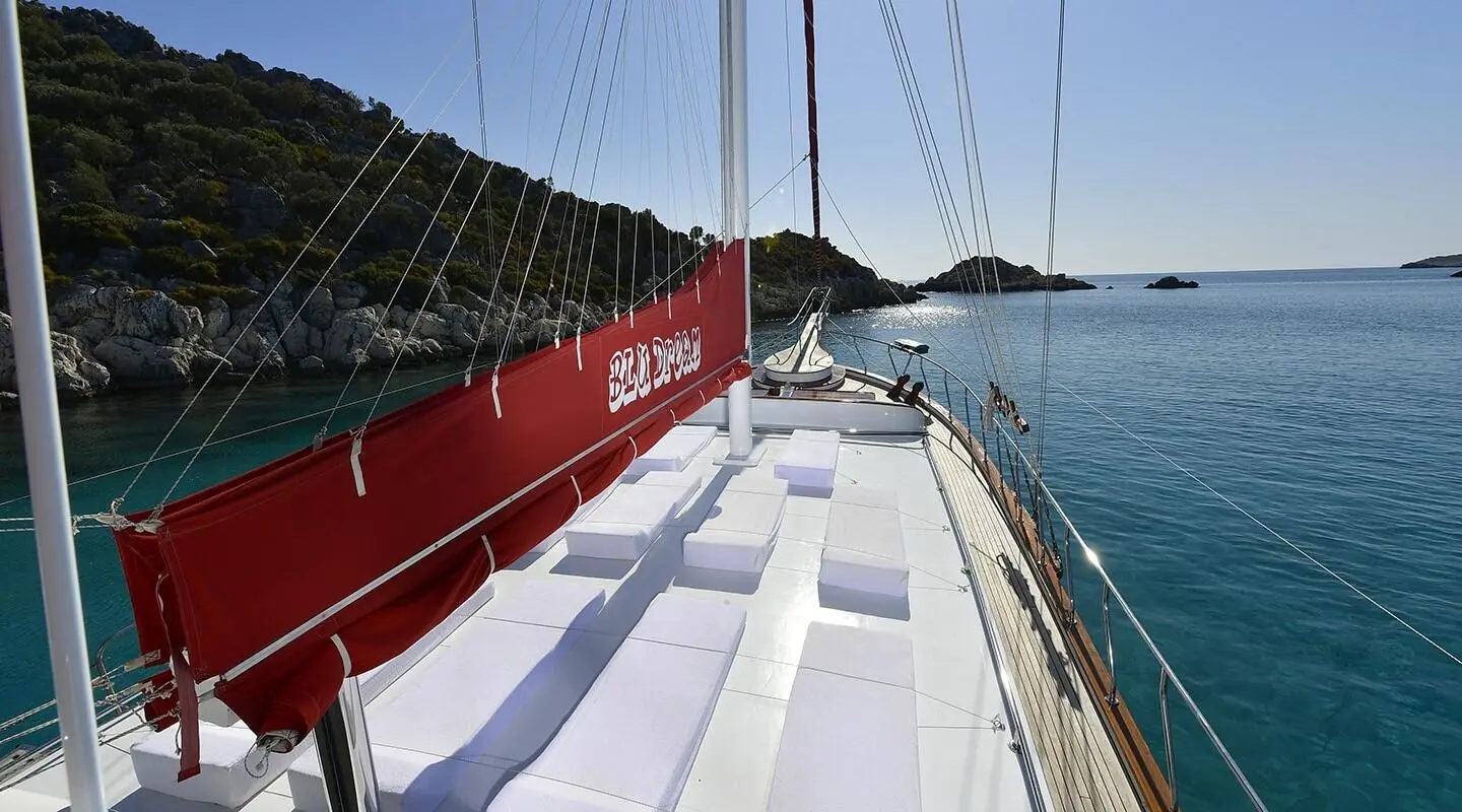 Red yacht hull with white deck, calm blue sea, and clear sky during sunset