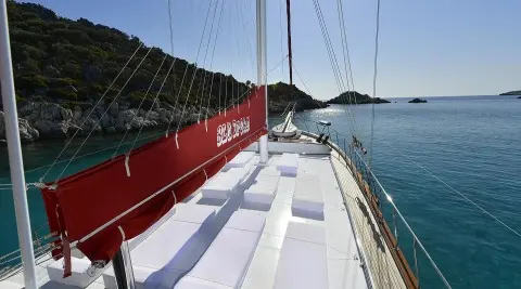 Red yacht hull with white deck, calm blue sea, and clear sky during sunset