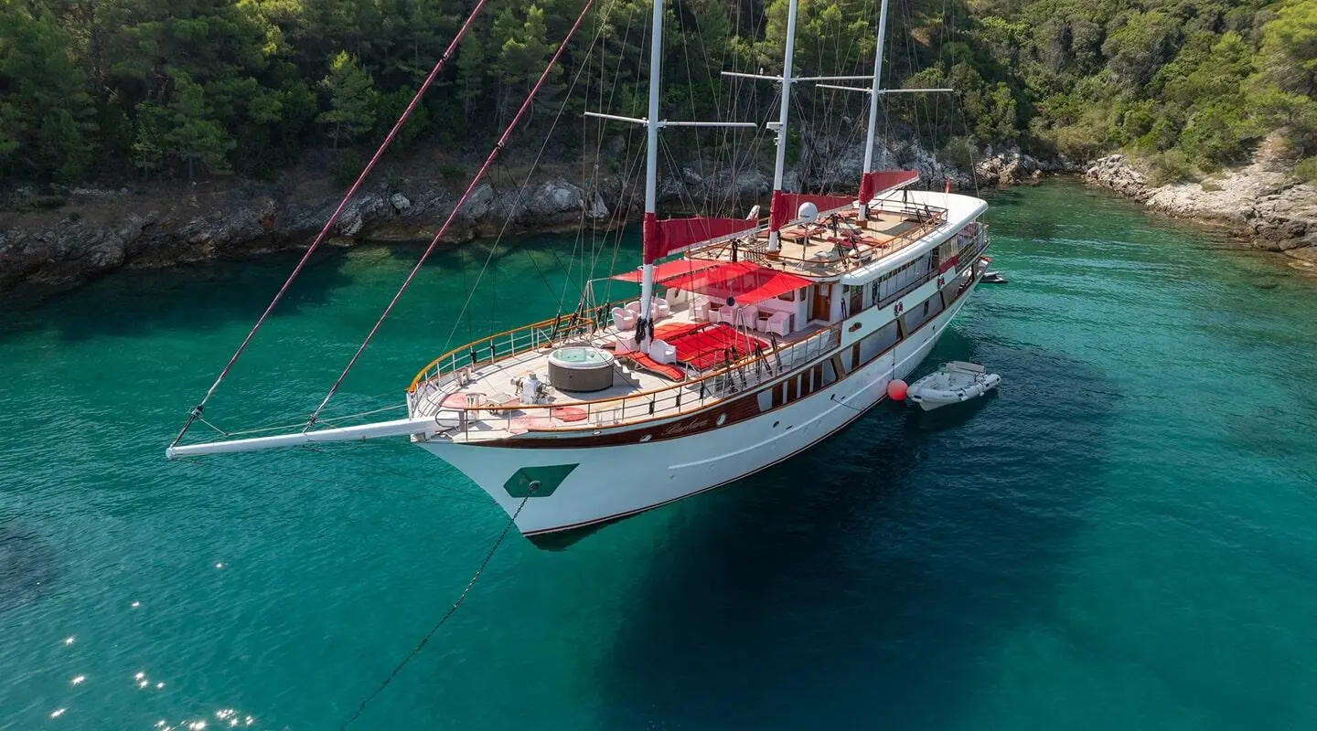 Yacht Barbara anchored in turquoise water with red seating and sails visible