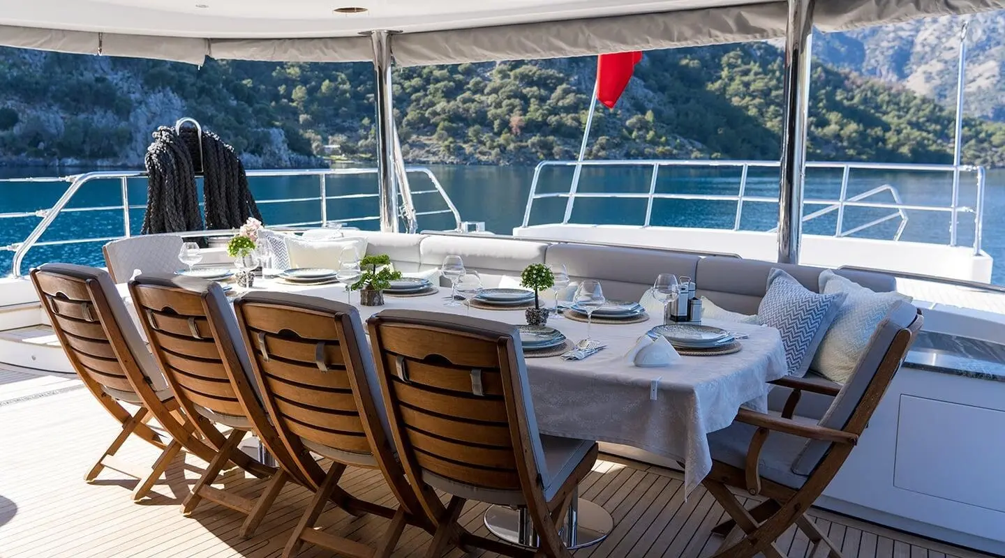 Long wooden chairs around a table on an open yacht deck over the sea