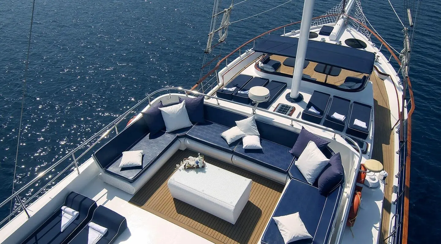 A luxurious yacht deck with cushioned seating, tables, and railing at sunset
