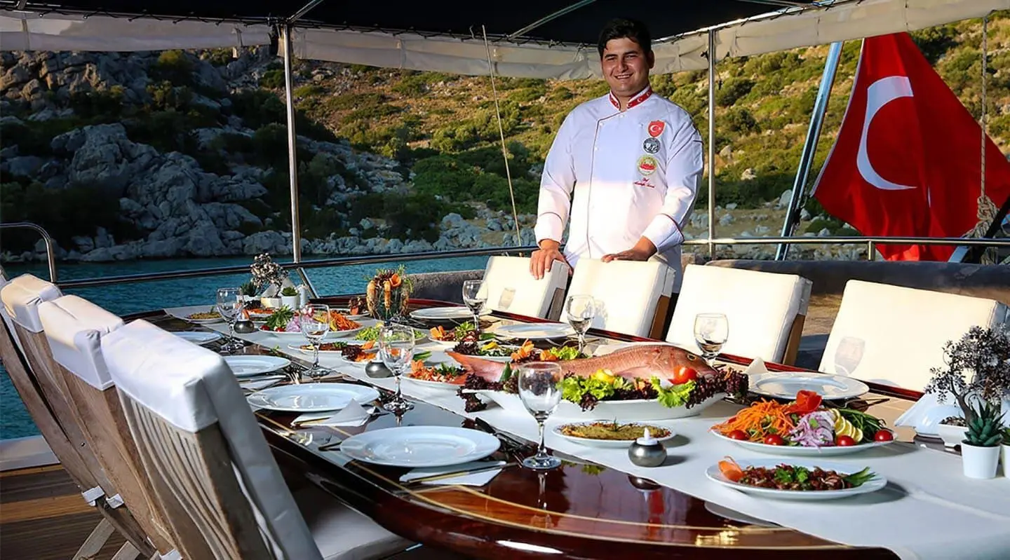 Diva Deniz yacht chef on deck with plates and sunset view over water