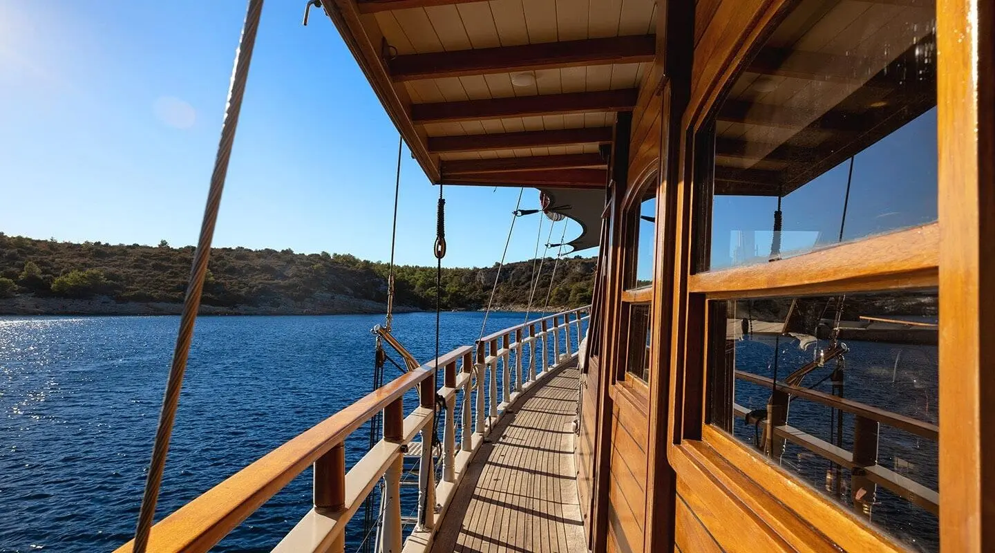 Aborda yacht deck with wooden railing along calm blue sea and rocky coastline
