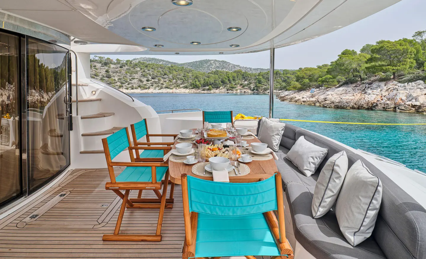 M Five motor yacht aft deck seating area with turquoise chairs and wooden table