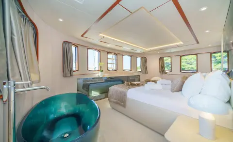 Maia yacht cabin with large bed, teal freestanding tub, and panoramic windows