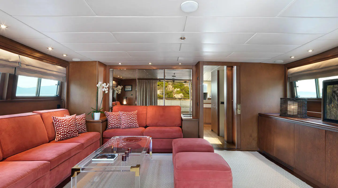 Idylle yacht interior with red sofa seating, wooden cabinetry, and large windows