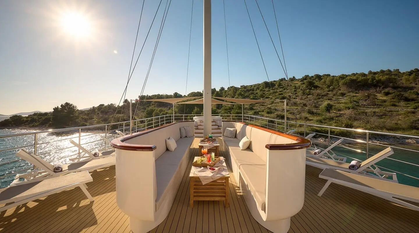 Bellezza yacht deck with sun loungers, table, and sailing rig under clear blue sky