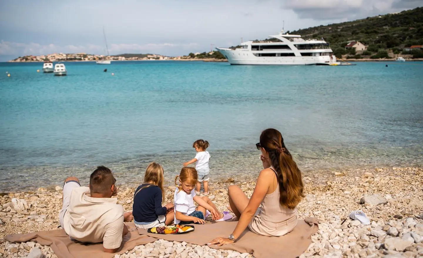 Karizma yacht anchored near shore with a family having a picnic on the rocky beach