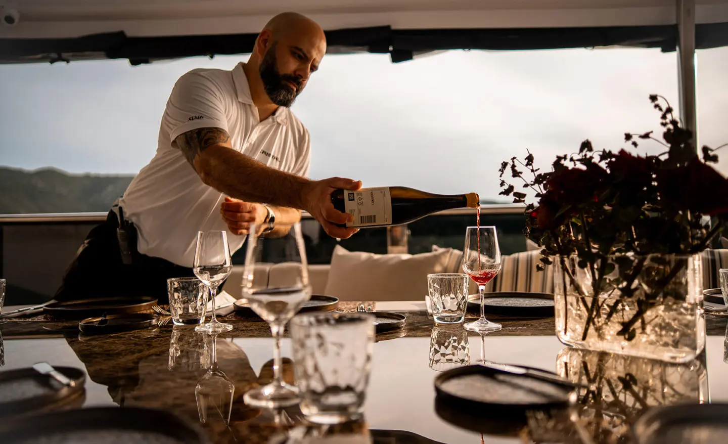 Cristal yacht waiter pours champagne at a sunlit teak dining table on deck