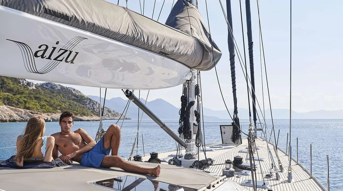 Sailing yacht Aizu with rigging, deck loungers, and crew on board under clear blue sky