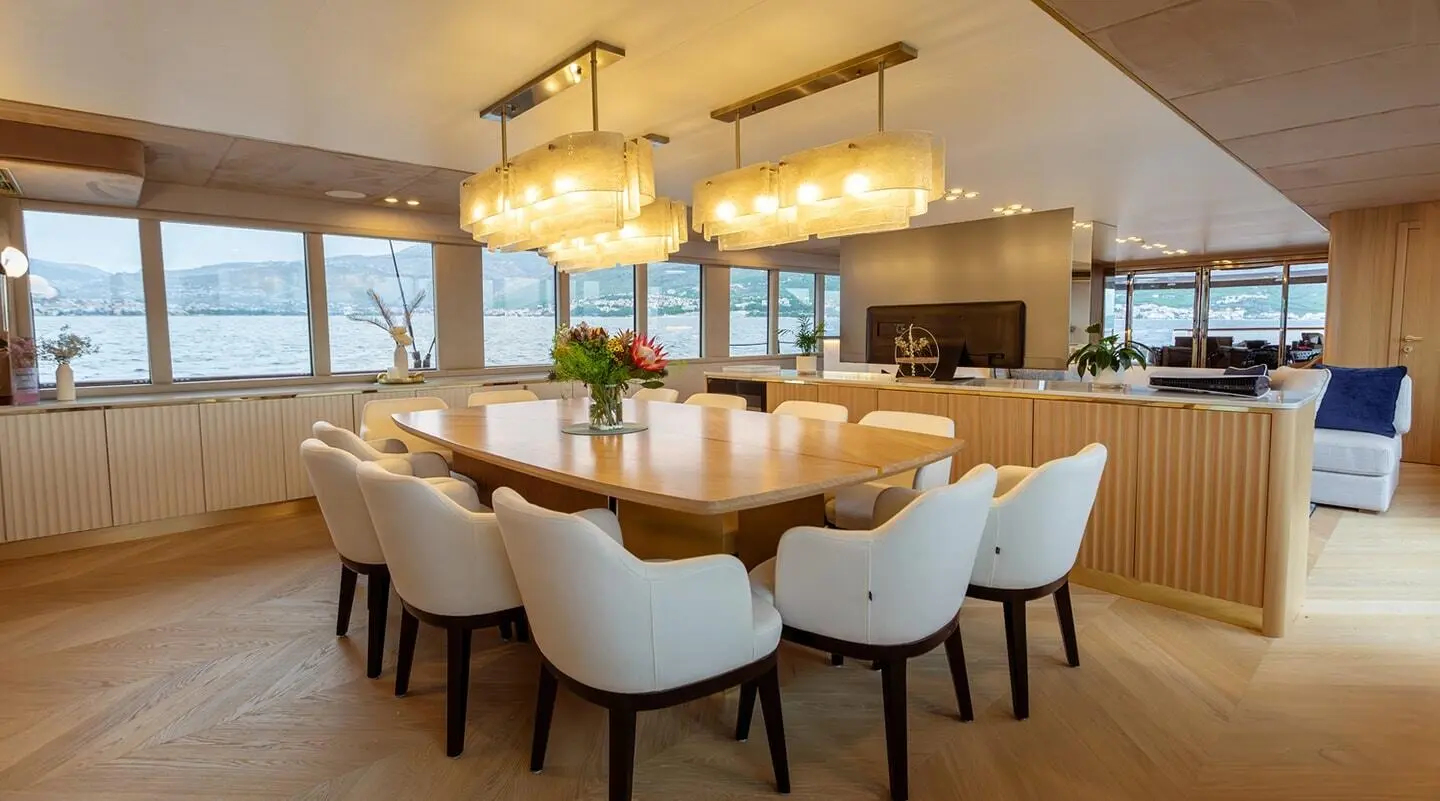 Scorpios luxury yacht dining salon with long light wood table and white upholstered chairs