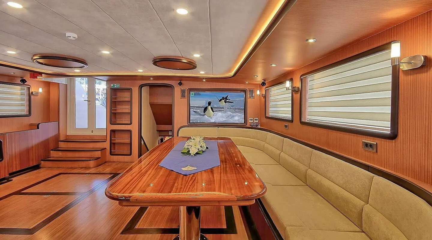 Queen Of Salmakis yacht interior with wooden table and beige seating aboard at dusk