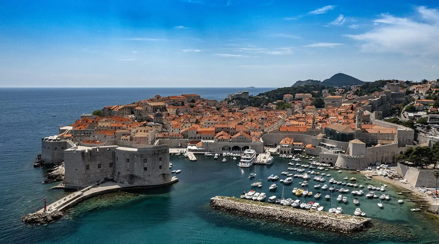 Yolo yacht docked in Dubrovnik harbor with buildings and boats nearby