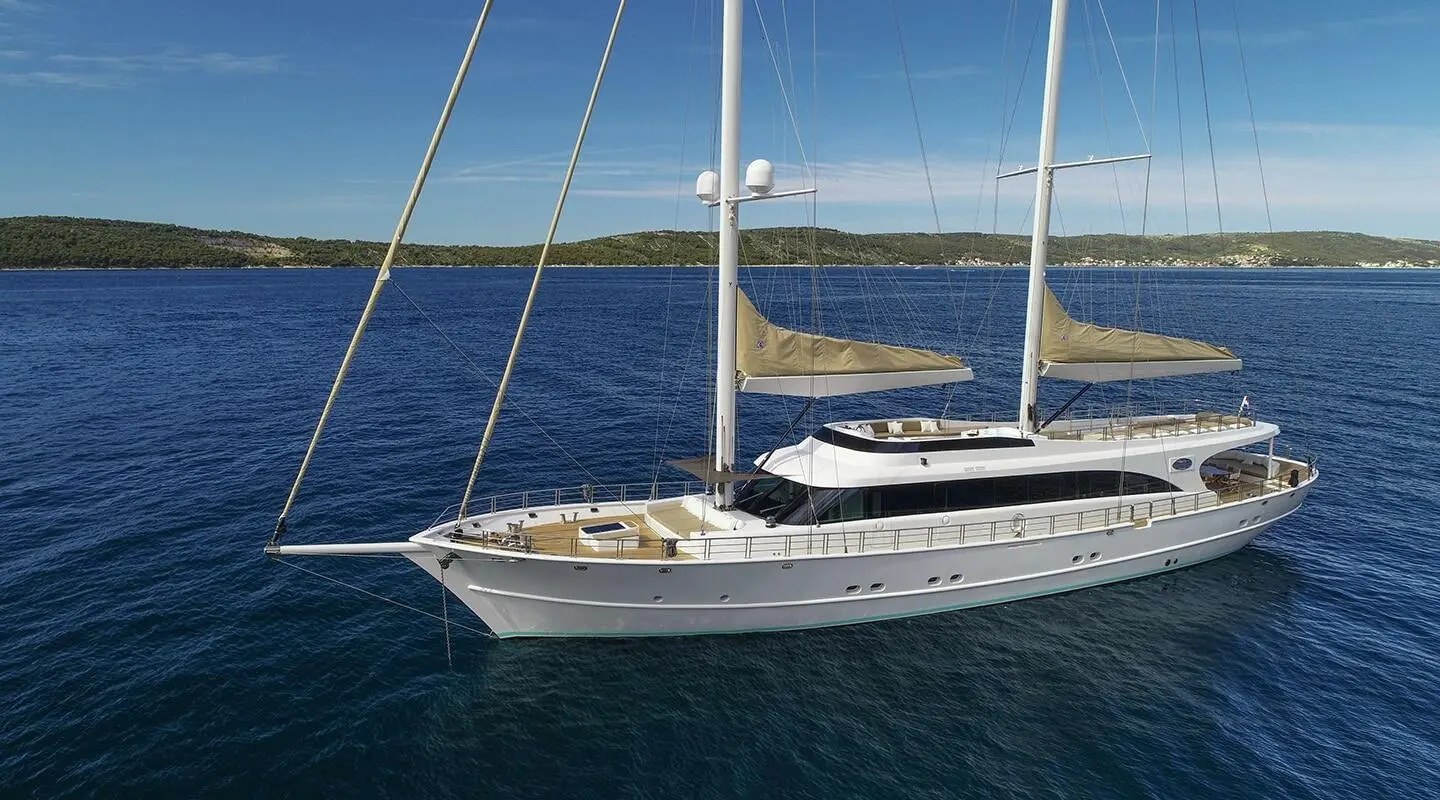 Sleek white sailing yacht Acapella anchored with sails furled beside calm blue sea