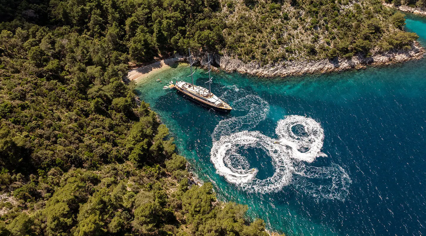 Dalmatino yacht anchored in blue sea near rocky coastline at sunset