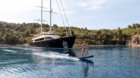 Nocturno yacht anchored near rocky shore at sunset with calm water